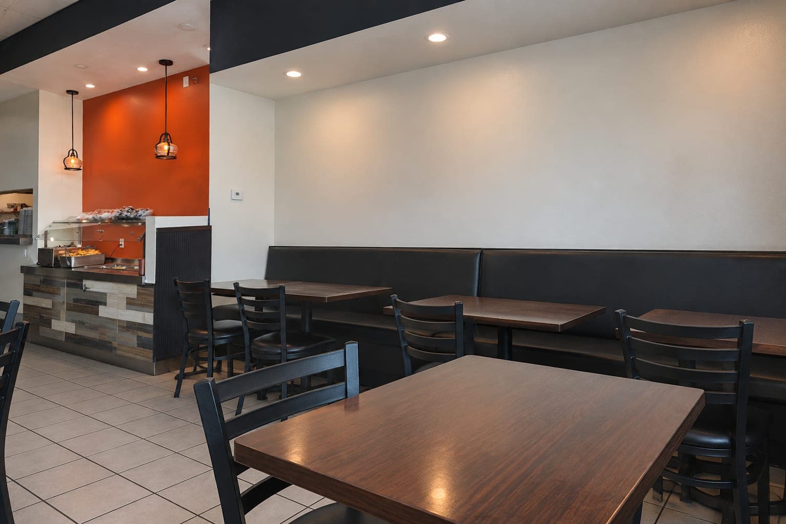 A warm dining room with dark tables, black chairs, and orange accents.