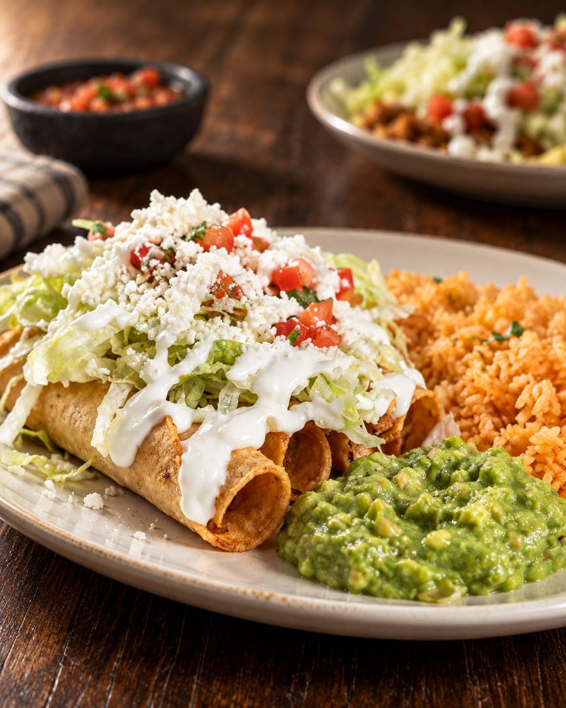A plated meal with crisp rolled tortillas, seasoned rice, guacamole, and fresh toppings.